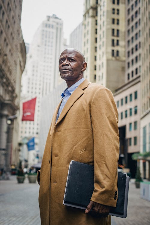Serious mature black man in overcoat with folder on street