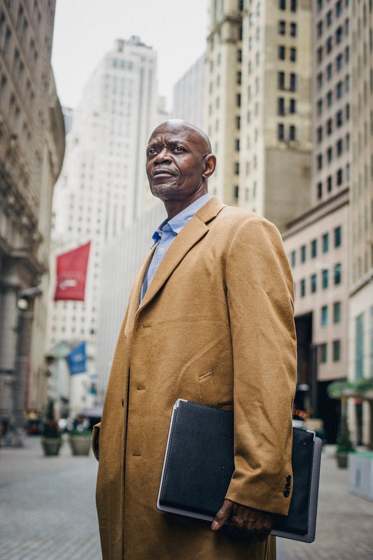 Serious Mature Black Man In Overcoat With Folder On Street