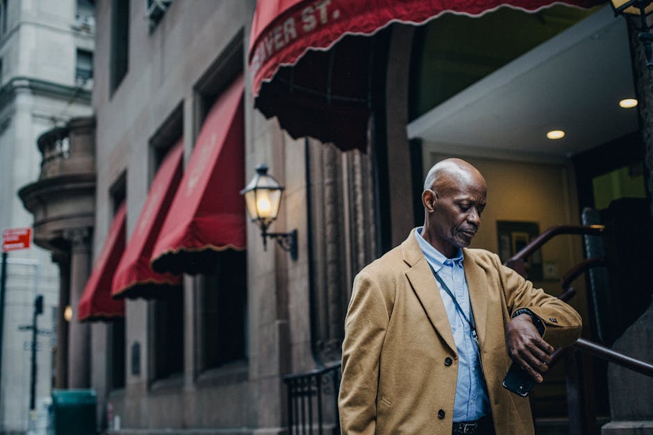 SoFi vs Marcus: Emergency Fund Growth Showdown Man in a tan coat checks his watch outside a classic city building with red awnings.