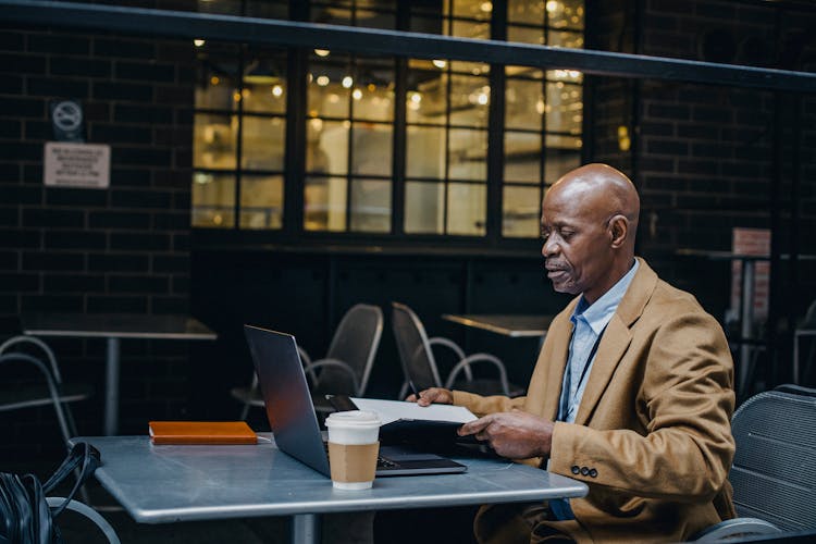 Thoughtful Black Man Browsing Laptop And Opening Documents In Cafe