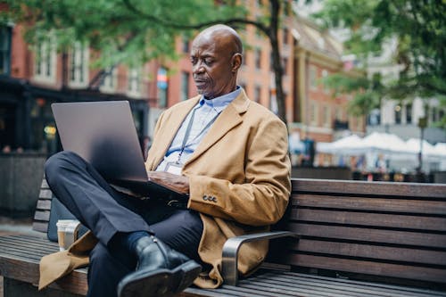 Serious African American executive watching laptop on bench in town