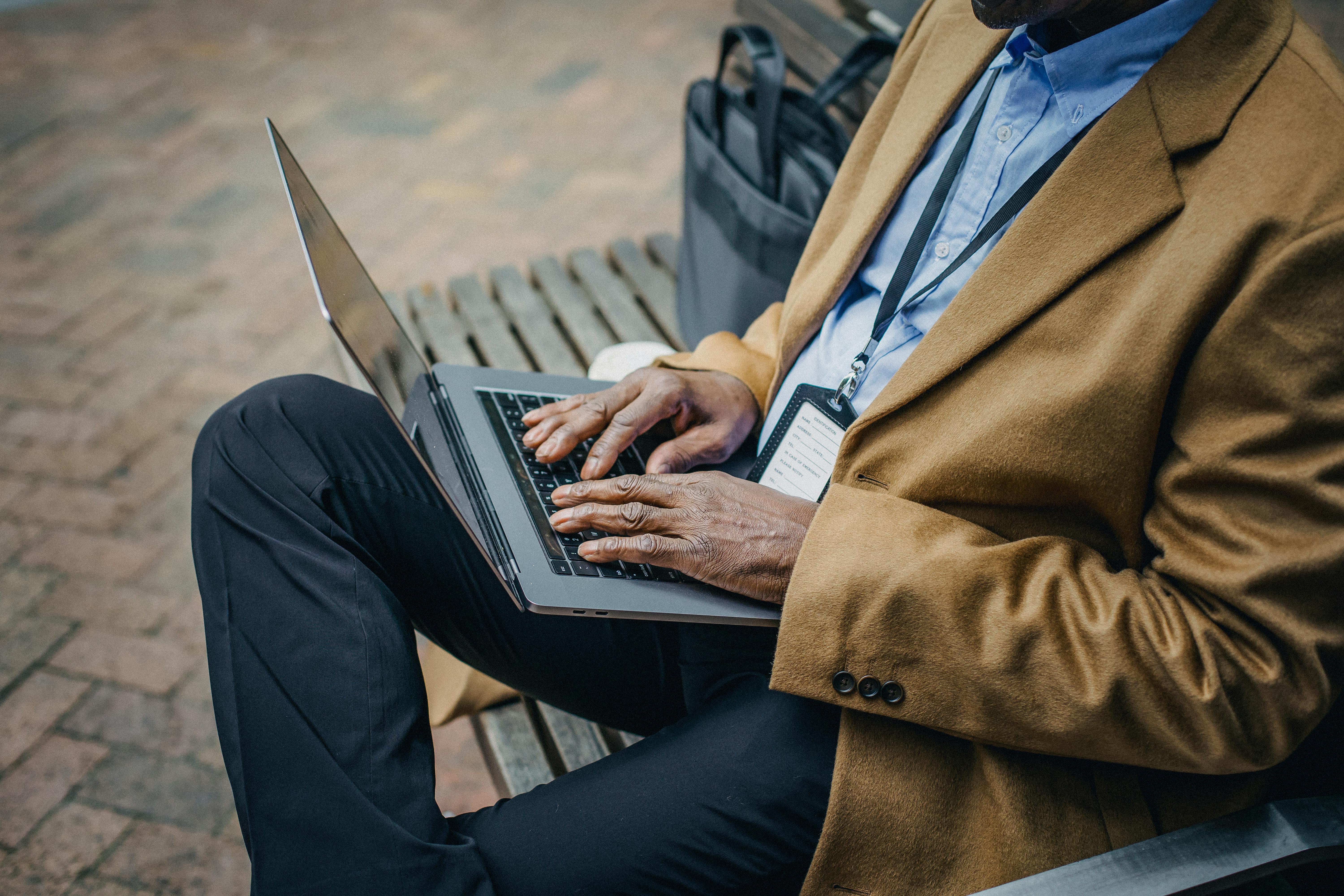 crop black businessman typing on laptop on street bench