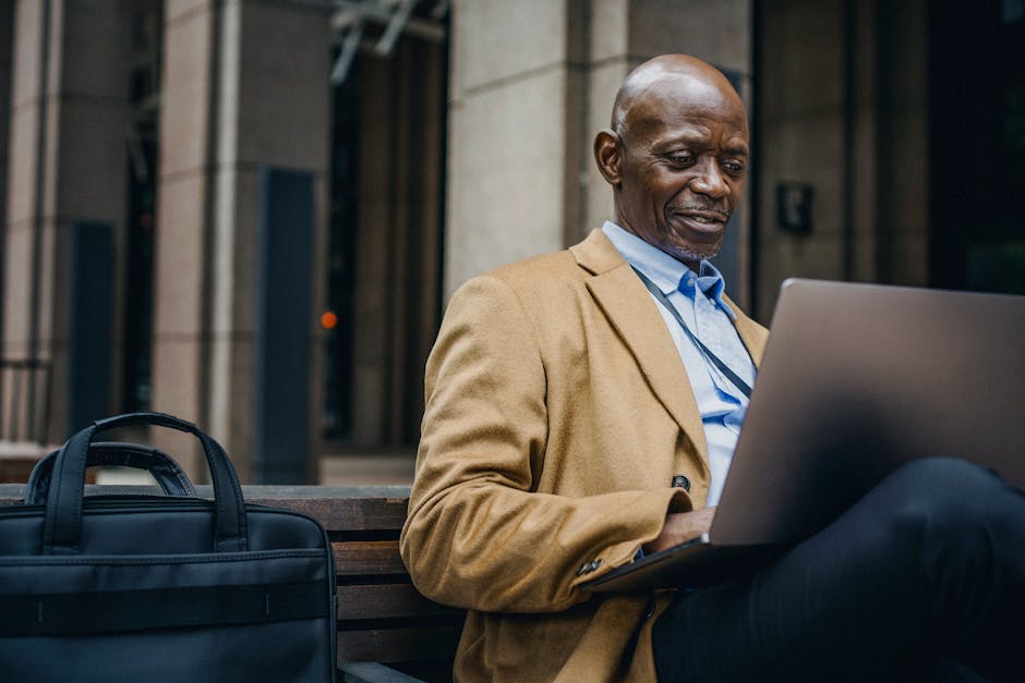 Smiling black businessman browsing internet on laptop in city