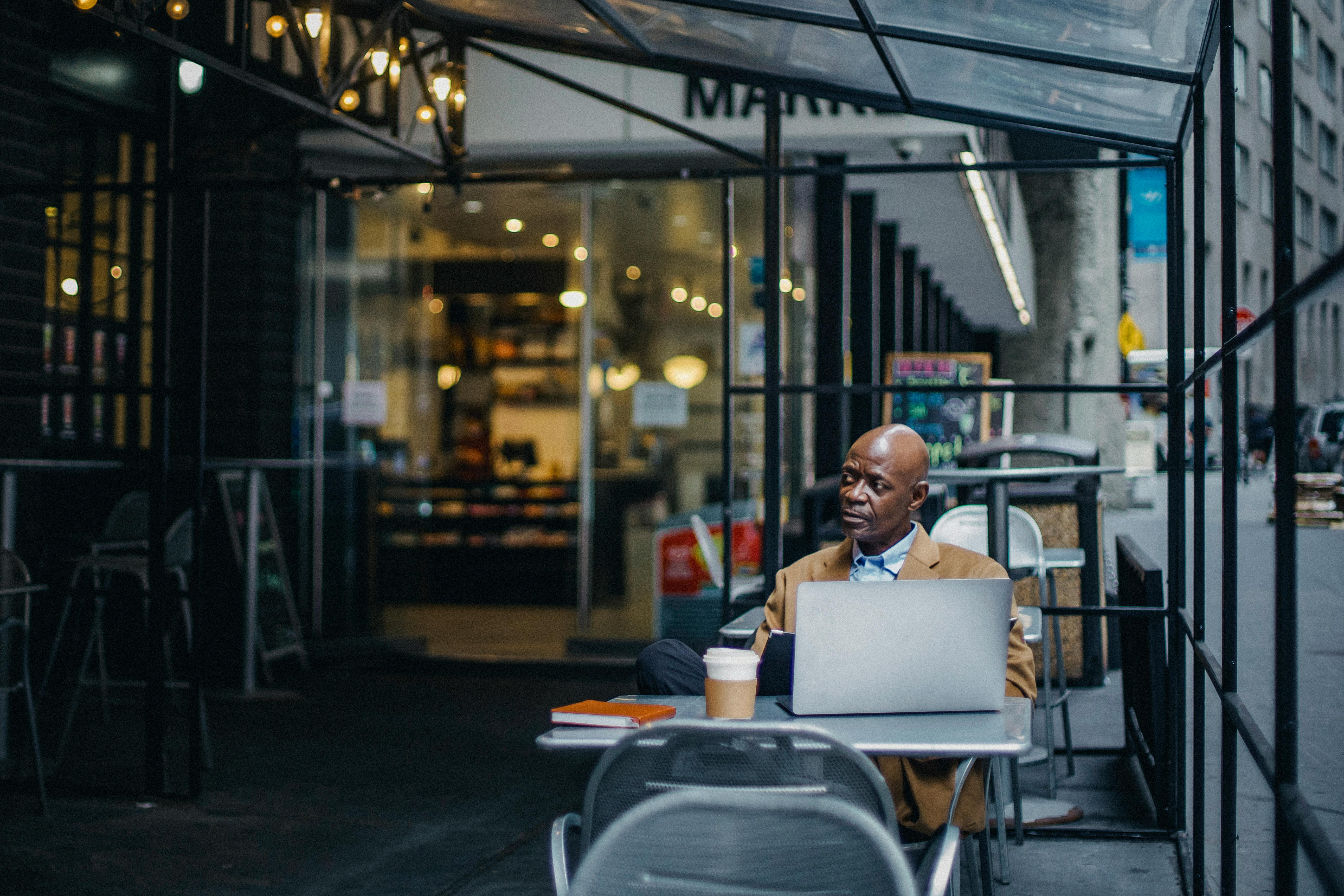 focused black businessman with laptop sitting in outdoor cafeteria