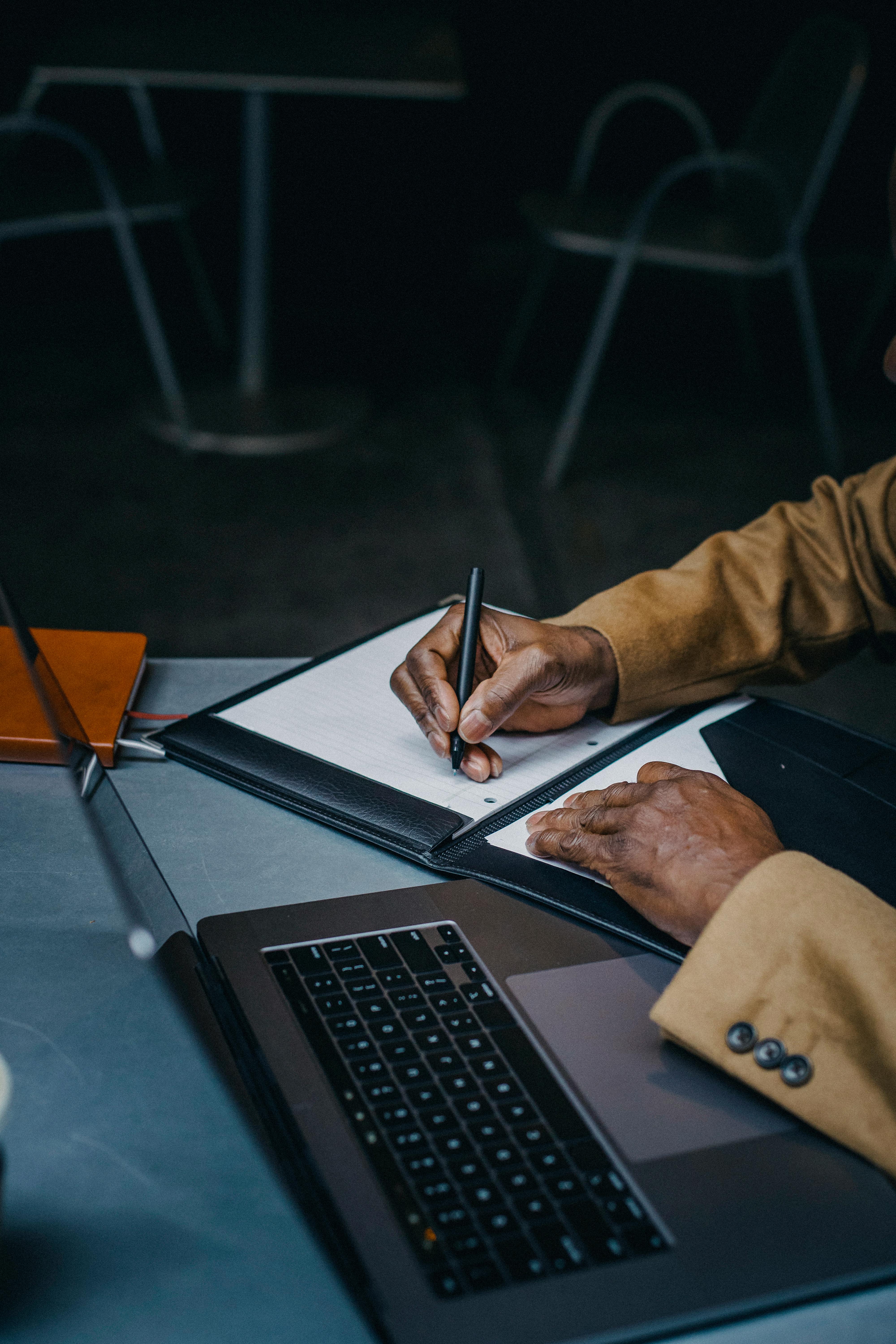 crop faceless black man working on laptop and taking notes