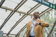 Serious African American businessman in formal clothes standing in subway station and checking time on wristwatch while looking away thoughtfully