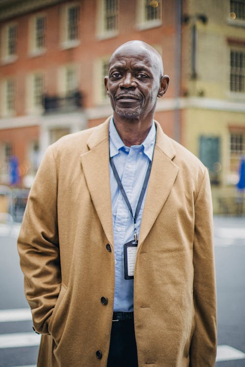 Confident adult African American businessman in elegant formal clothes standing on urban street and looking at camera