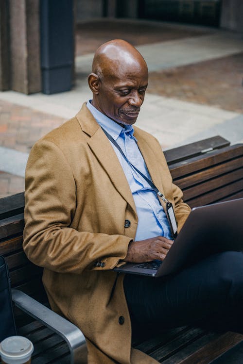 Free Black businessman using laptop on street bench Stock Photo