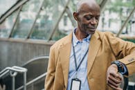 Crop punctual African American male in elegant formal clothes standing near metro entrance and checking time on wristwatch