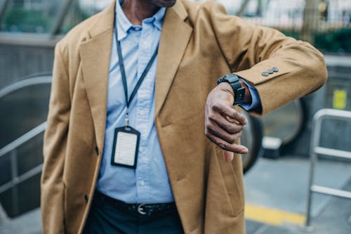 Free Crop anonymous African American businessman in elegant formal suit looking at wristwatch while standing near metro entrance Stock Photo