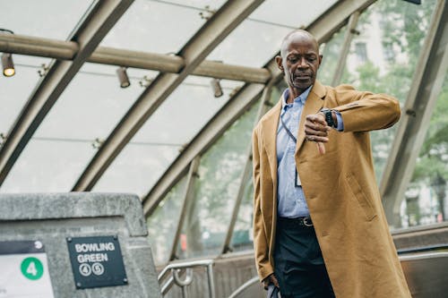 Free Pondering black businessman looking at wristwatch near subway Stock Photo