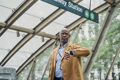 Обдумывая черный бизнесмен, проверяющий время на наручных часах возле станции метро