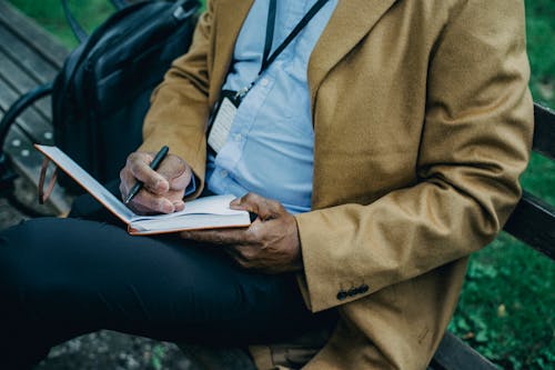 Free Crop faceless black businessman writing thoughts in notepad in park Stock Photo