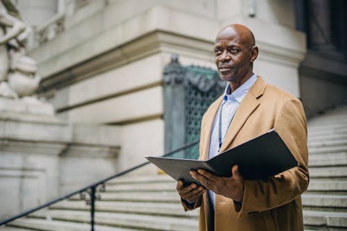 Serious black businessman reading documents in folder on building steps