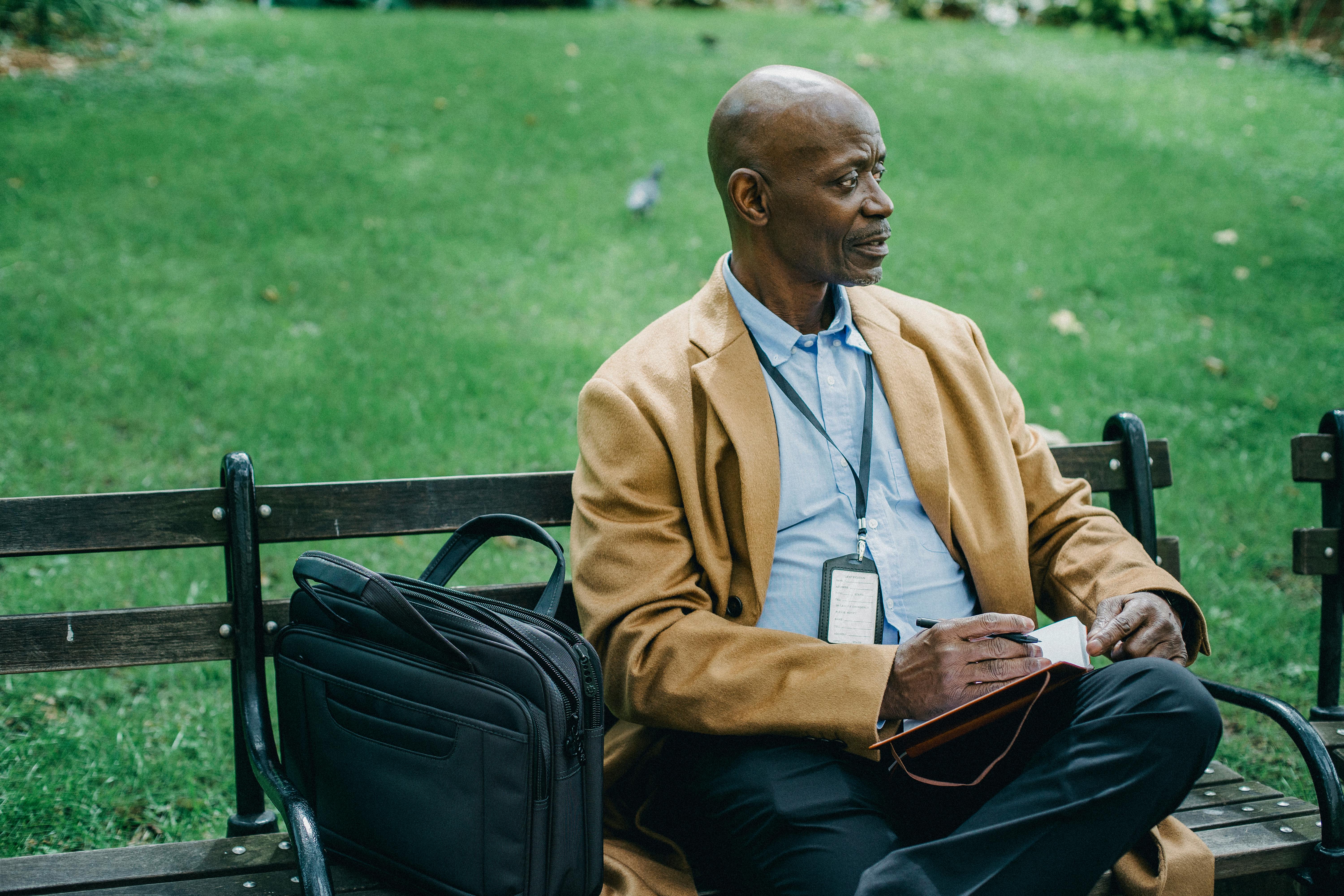 Pondering Black Man Sitting On Bench In Park With Notepad Free Stock   Pexels Photo 5648084 