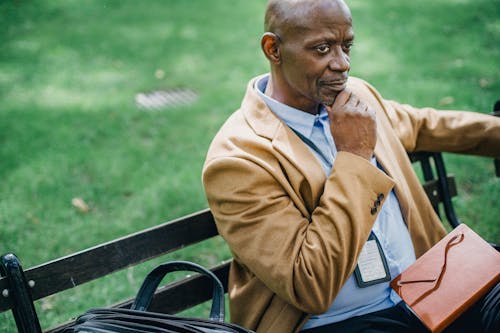 Crop thoughtful black manager with diary on street bench