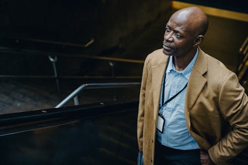 From above of wistful mature African American male executive with hand in pocket looking away on moving staircase