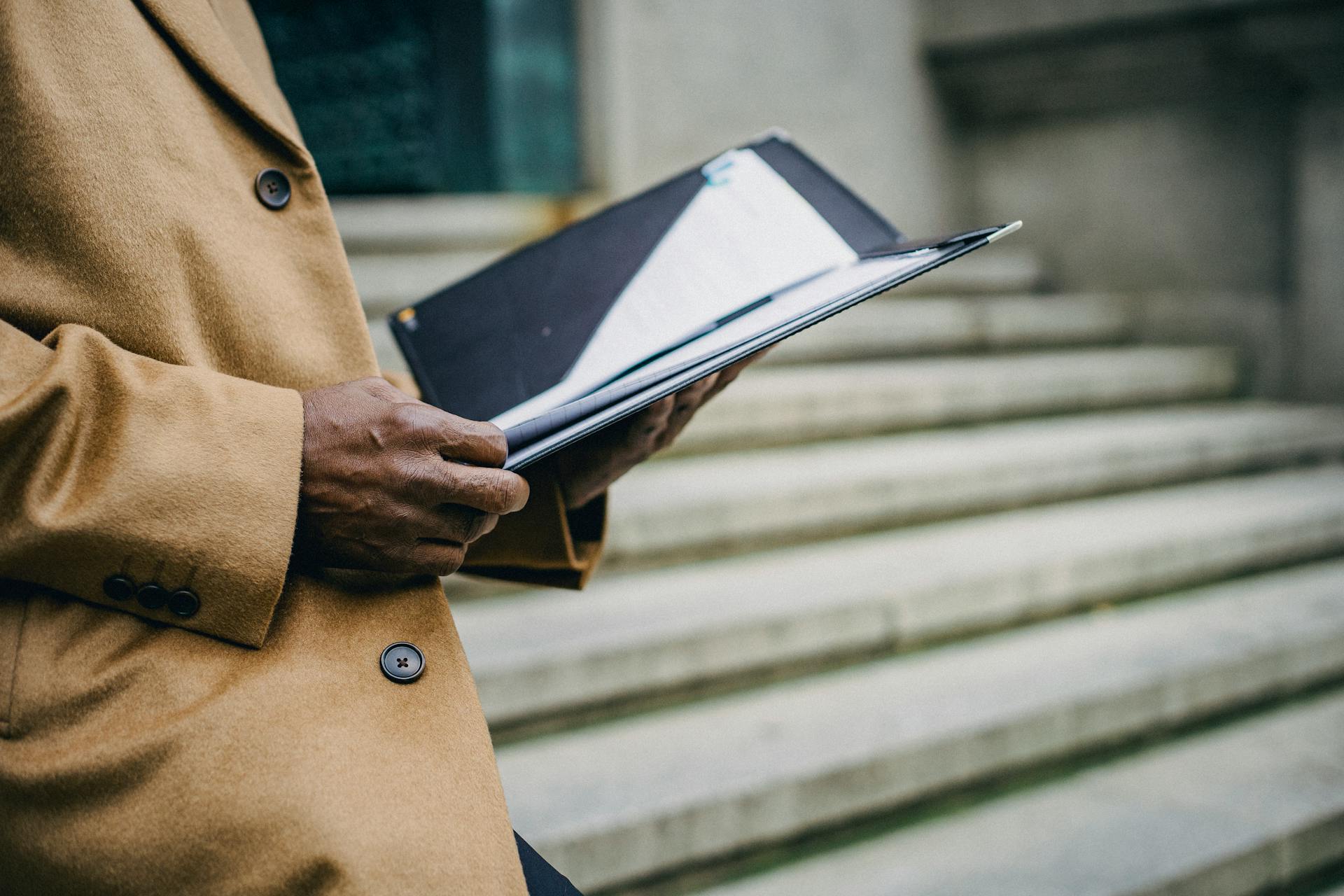 Stylish man in a coat holding a folder on city stairs, embodying professionalism.