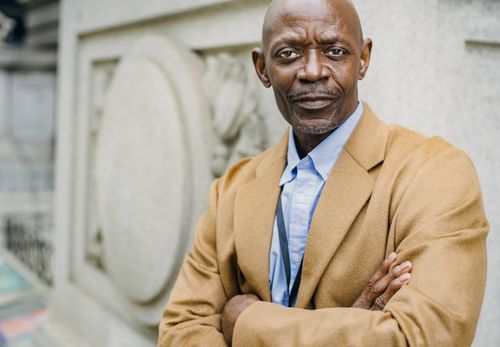 Free Crop serious middle aged black male in classy outfit standing near aged building with folded arms and looking at camera Stock Photo