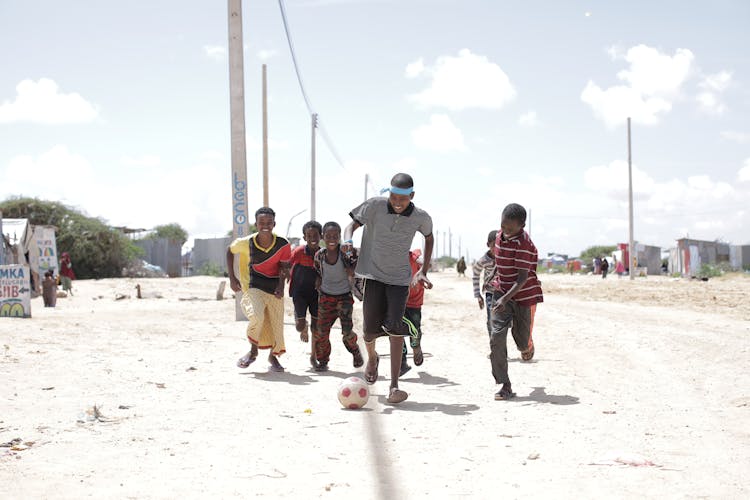 Group Of Children Playing Ball On Dirt Ground