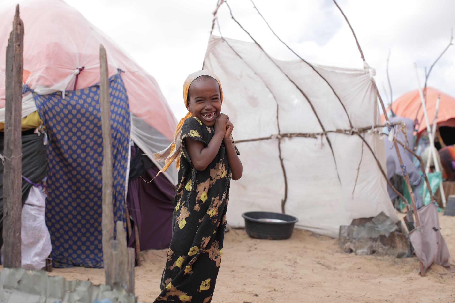 African girl smiling happily outside tents in a refugee camp.