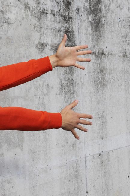 Hands in orange sleeves reaching against a concrete wall, symbolizing expression and freedom.