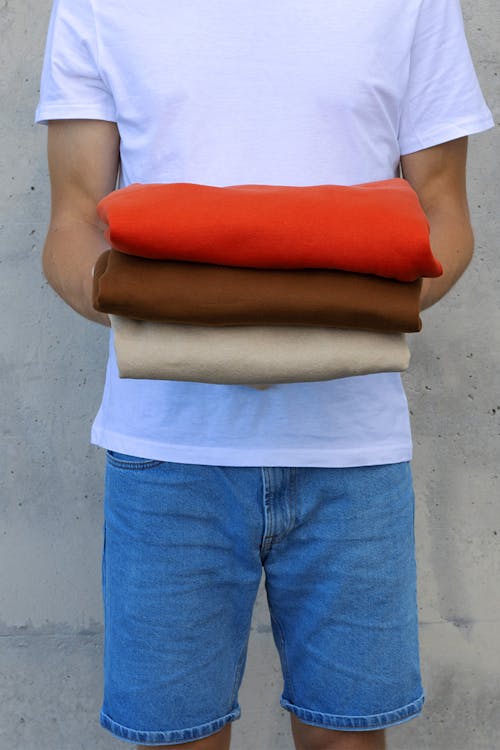 Person in White Shirt and Denim Shorts Holding Fabrics of Assorted Colors