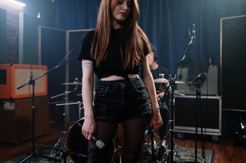Free Woman in Black Crop Top and Blue Denim Shorts Standing In A Music Studio With Microphone  Stock Photo