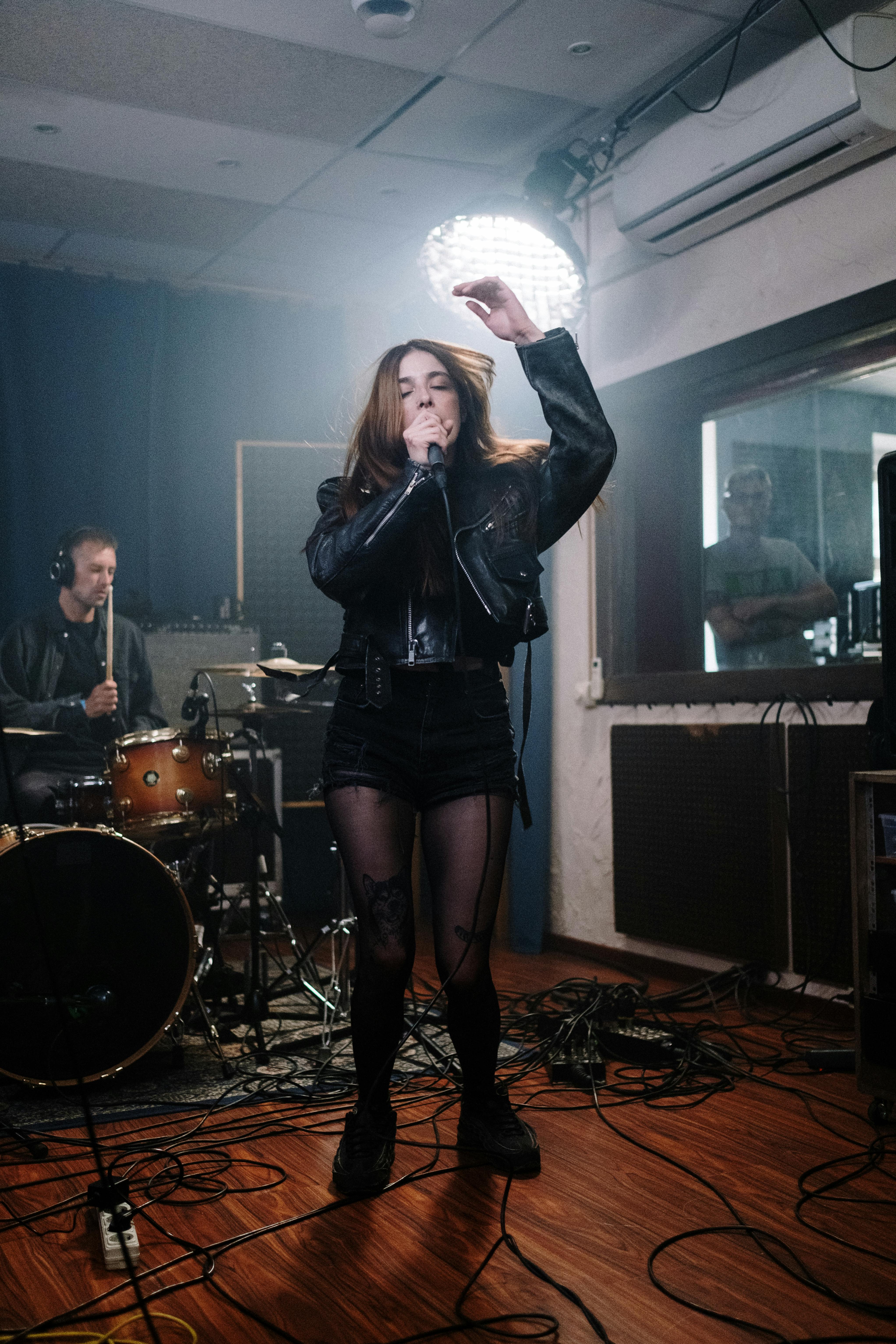 a woman singing wearing black leather jacket and black shorts