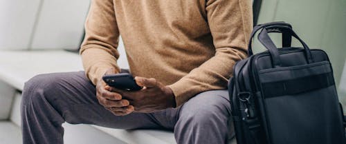 Anonymous ethnic guy surfing smartphone sitting on bench