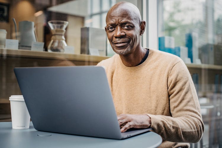 Smiling Middle Aged Black Man Working Remotely On Netbook In Cafe