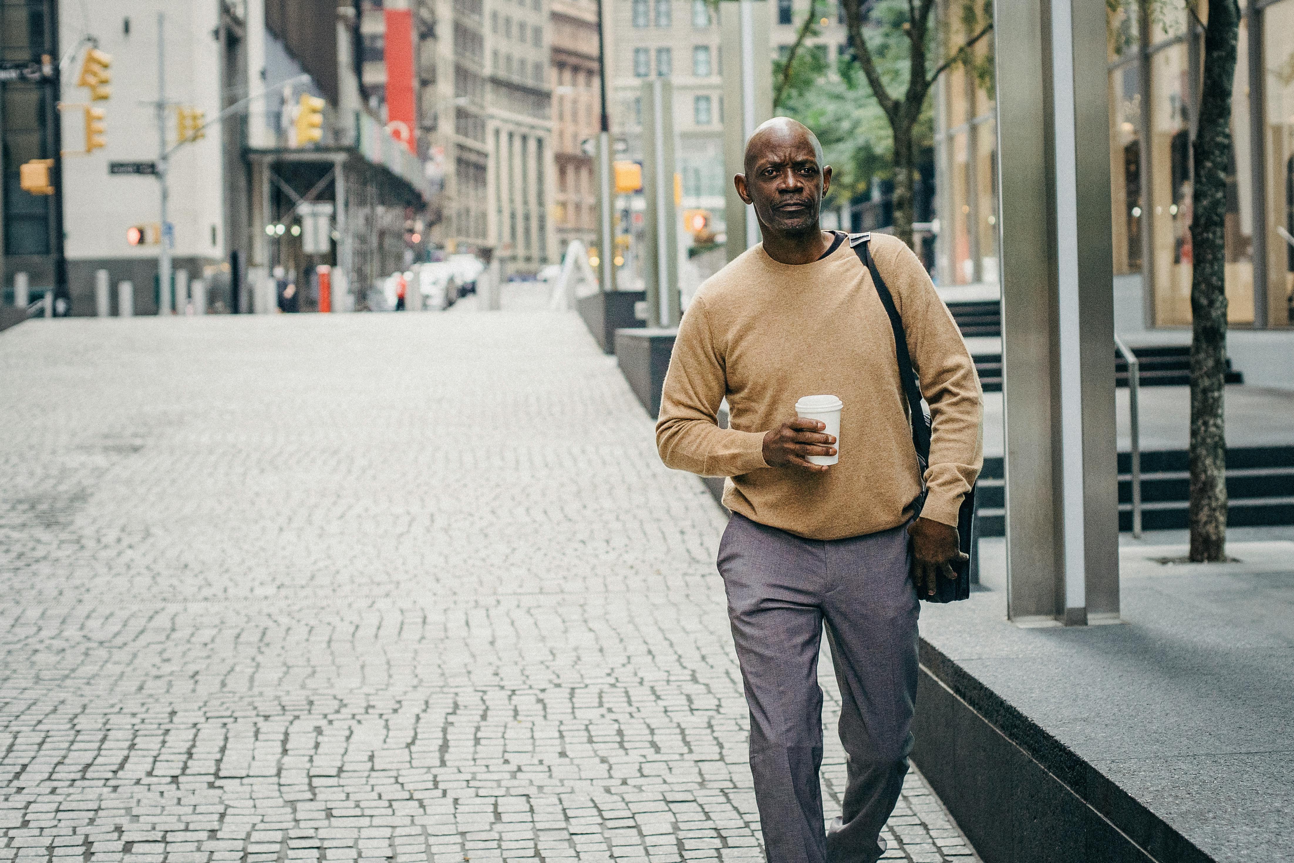 serious ethnic man strolling on paved street with coffee to go