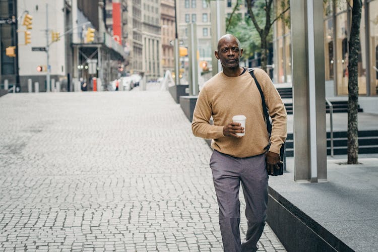 Serious Ethnic Man Strolling On Paved Street With Coffee To Go