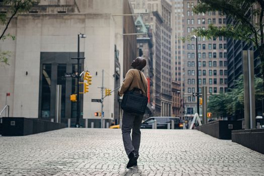 一名男子提着笔记本电脑包，走过繁华城市的鹅卵石街道