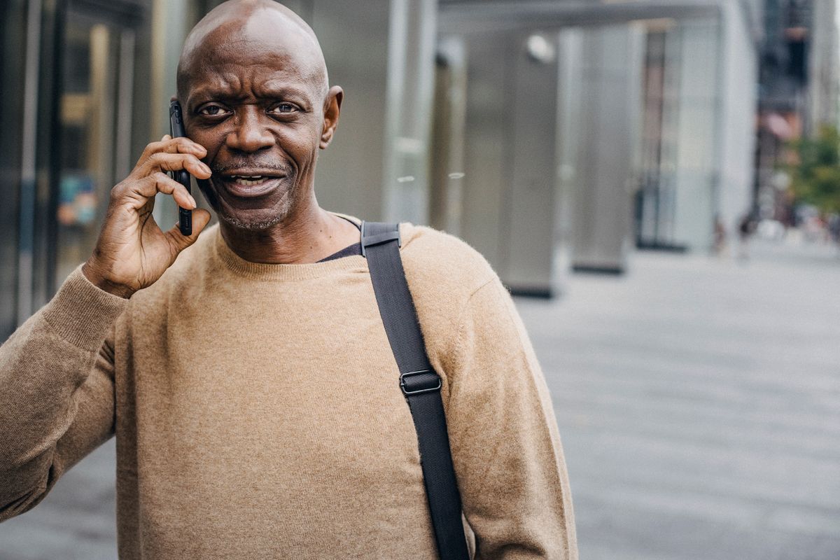 A man talking on his phone outdoors, booking a journey