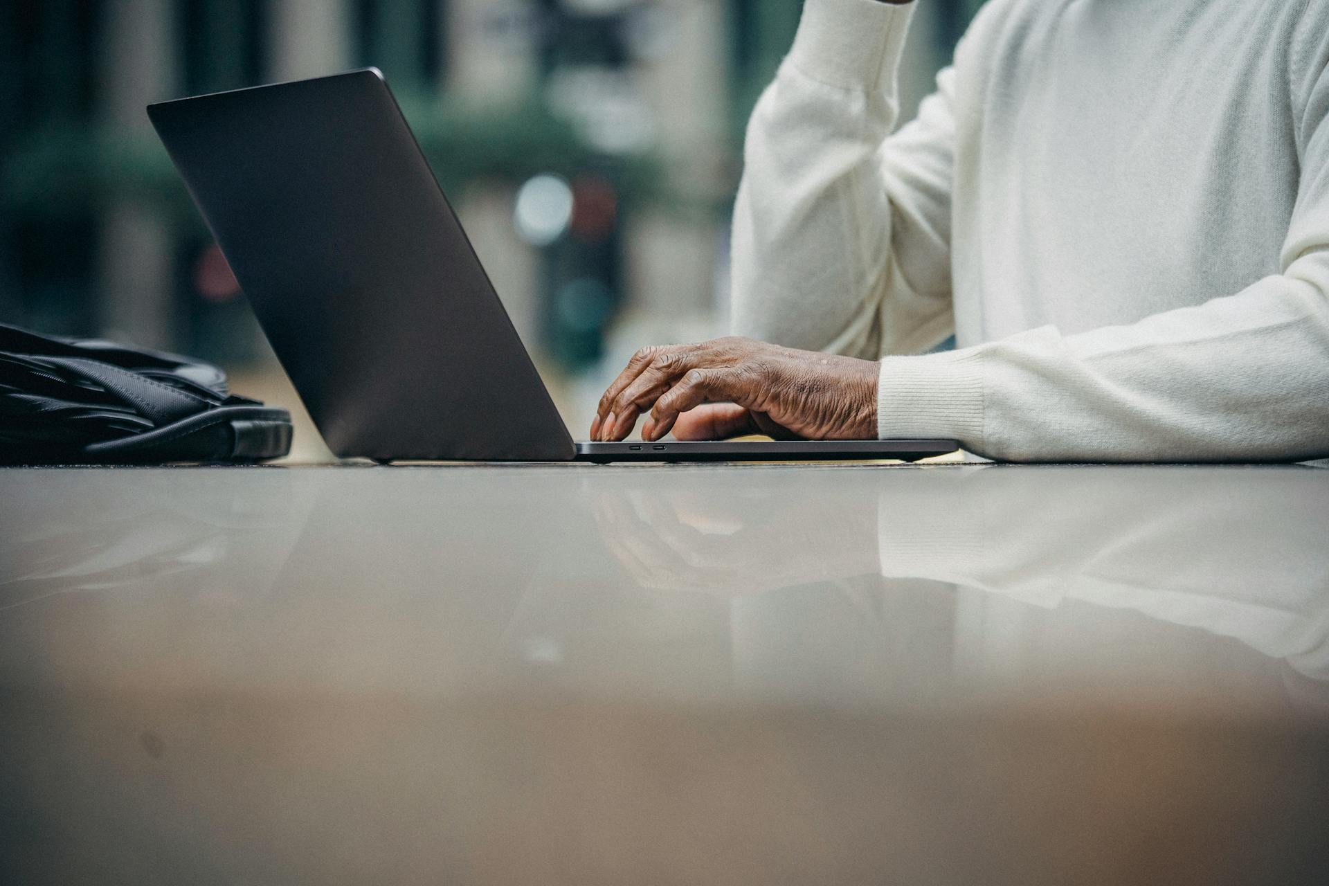 Low angle of crop anonymous mature black male freelancer typing on laptop keyboard while working remotely in outdoor cafe