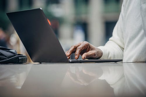 Free Unrecognizable black businessman working on netbook in street cafe Stock Photo