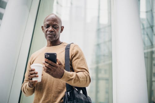 Focused mature black man chatting on smartphone during coffee break on street