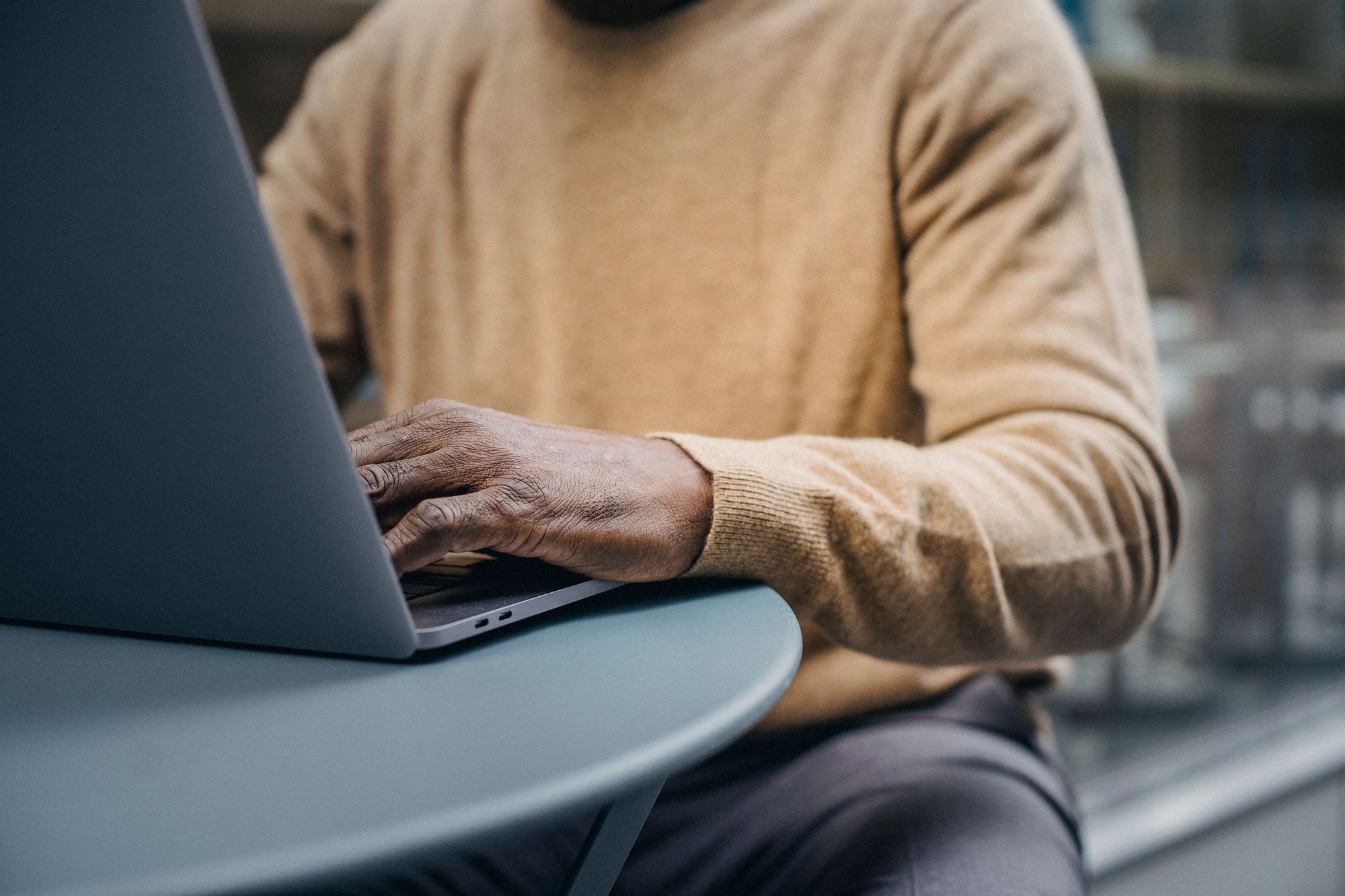 Periodista trabajando frente a una laptop en una redacción con varias pantallas al fondo
