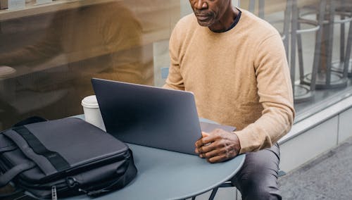 Crop thoughtful black man working on netbook in street cafeteria