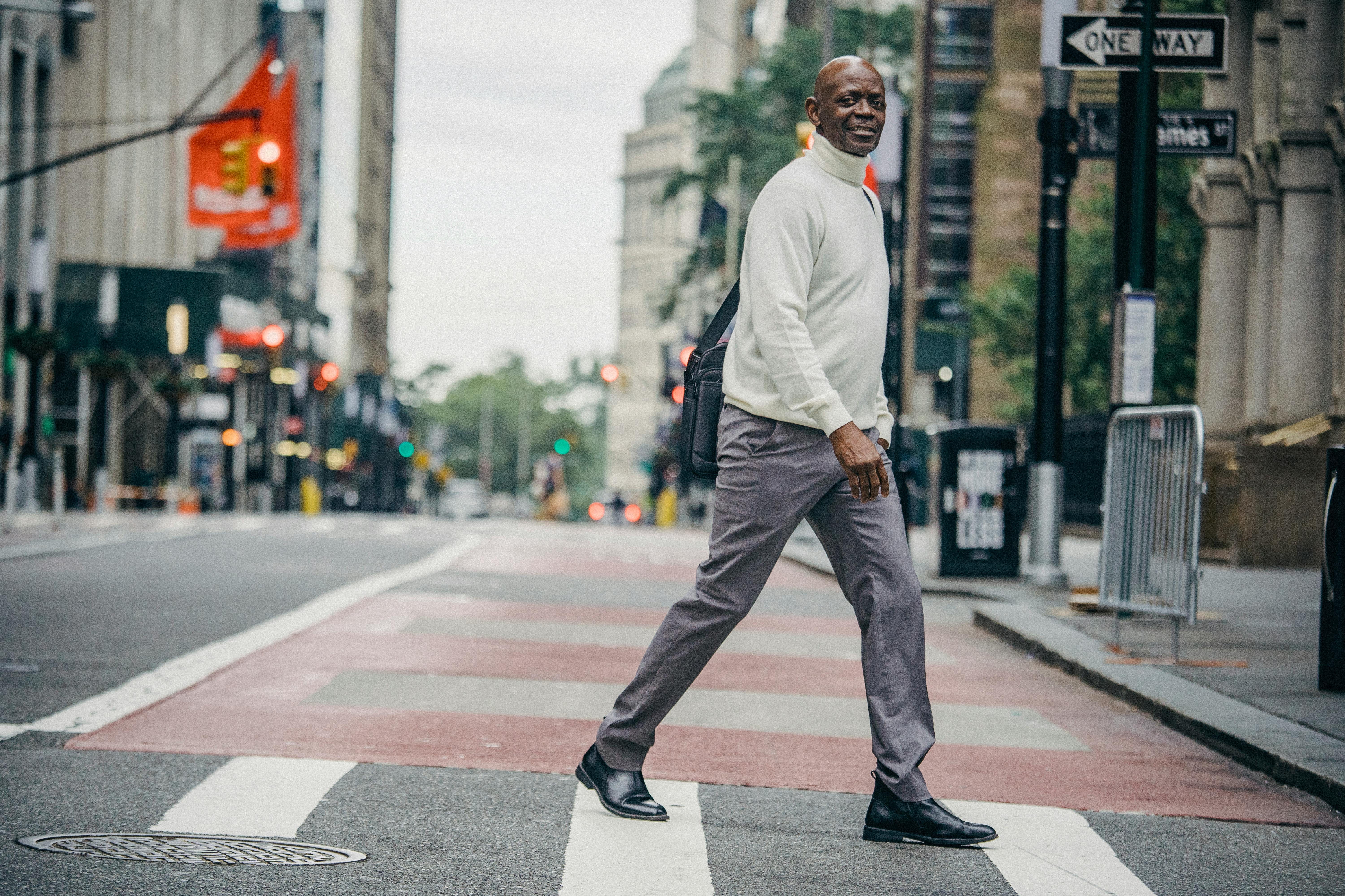 一位衣着优雅、面带微笑的成熟非裔美国男性，正从市中心过马路的侧面视图