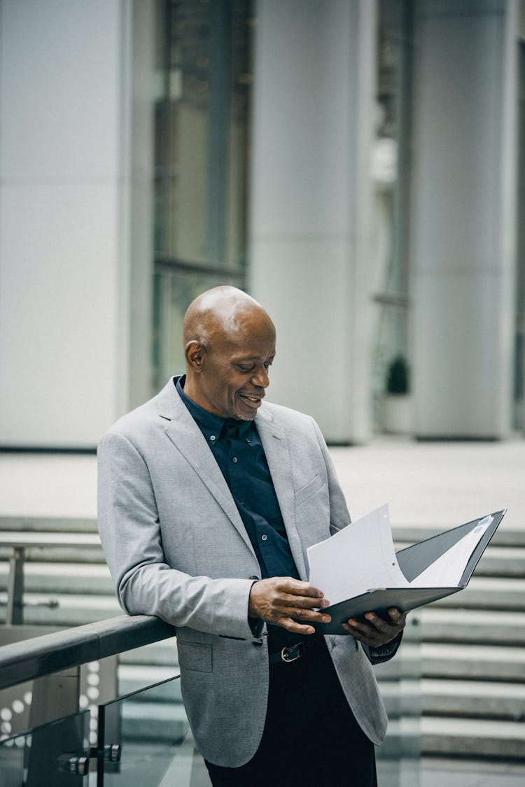 Positive Mature Black Businessman Reading Documents Leaning On Railing