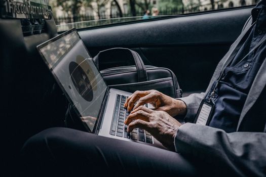 Businessman typing on a laptop inside a car, showcasing remote work lifestyle.