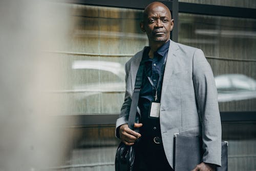 Serious black businessman with bag standing near building wall