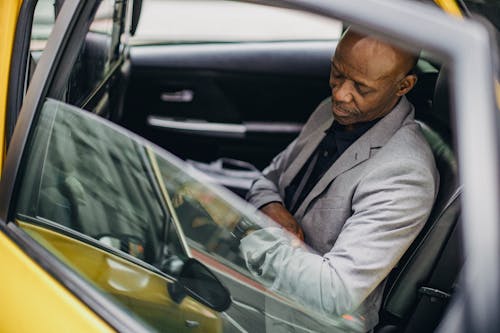 Free Side view punctual adult African American businessman in formal clothing sitting in taxi car and checking time on wristwatch Stock Photo