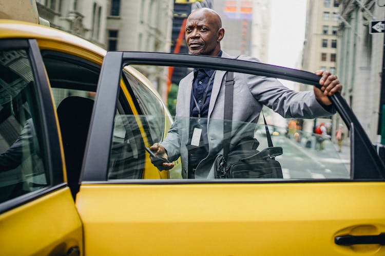 Black Businessman Opening Taxi Door In Modern City