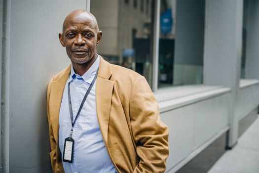 一位身着西装的非裔美国商人，正若有所思地靠在现代建筑的墙壁上，凝视着镜头