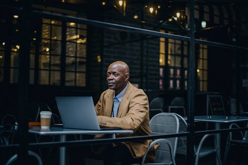 Man In Brown Jacket Sitting In Front Of Macbook