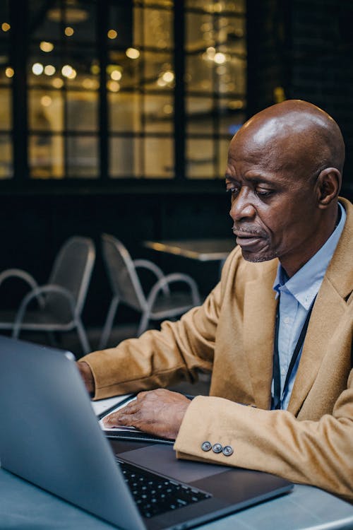 Free Focused well dressed mature African American male executive working on project on netbook at cafe table Stock Photo