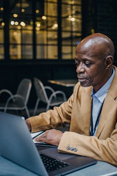 Focused well dressed mature African American male executive working on project on netbook at cafe table